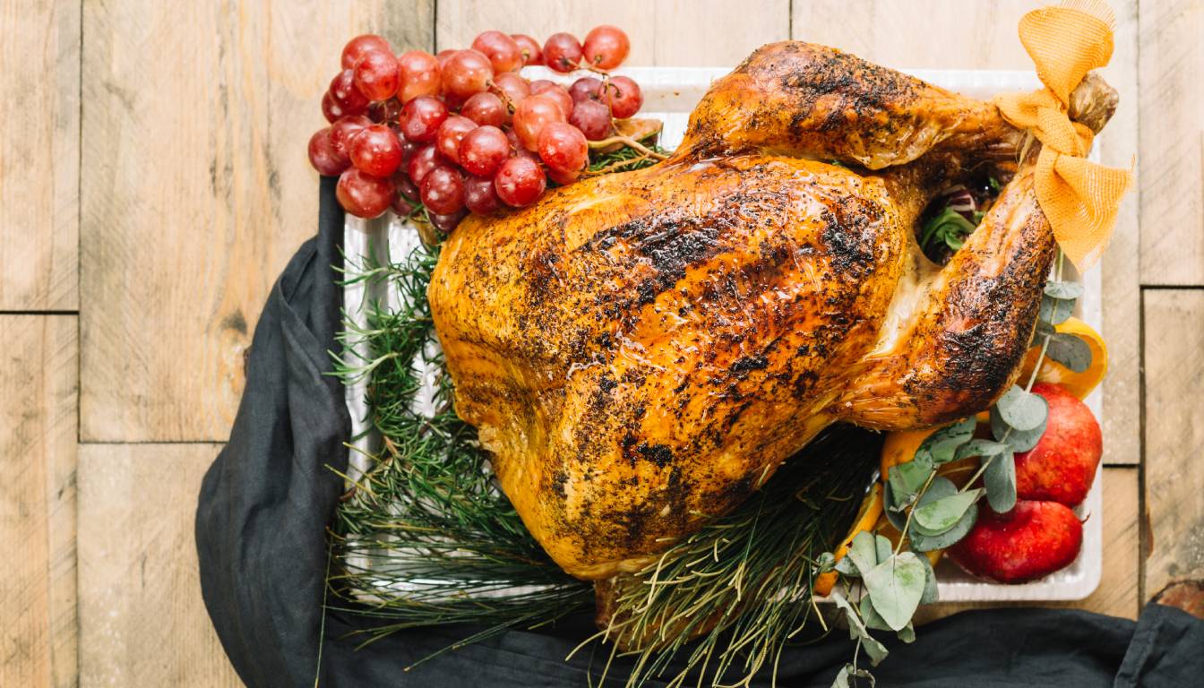 A beautifully roasted turkey garnished with fresh herbs, red grapes, and apples, presented on a wooden table.