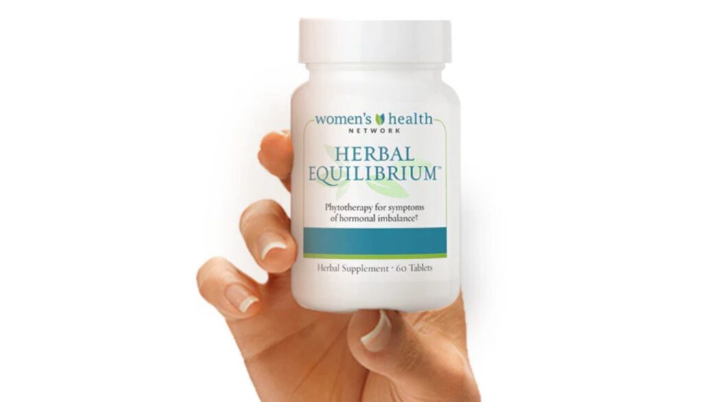 A hand holding a bottle of Women's Health Network Herbal Equilibrium supplement, which is designed to address symptoms of hormonal imbalance. The bottle contains 60 tablets.