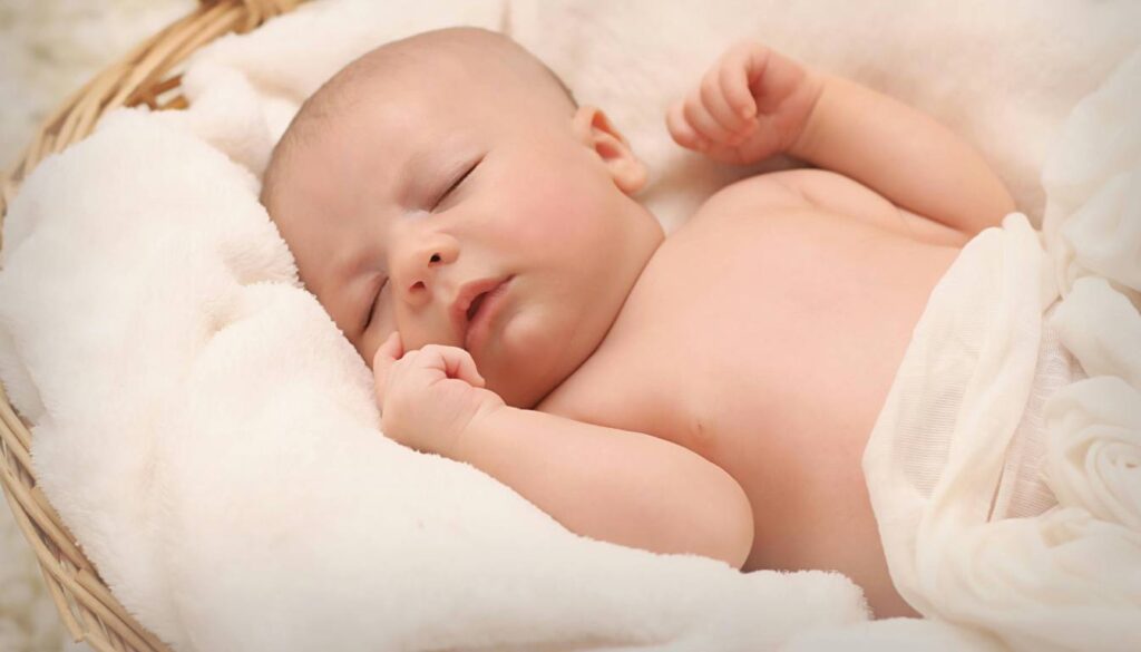 A baby lying on a bed with a humidifier in the background.