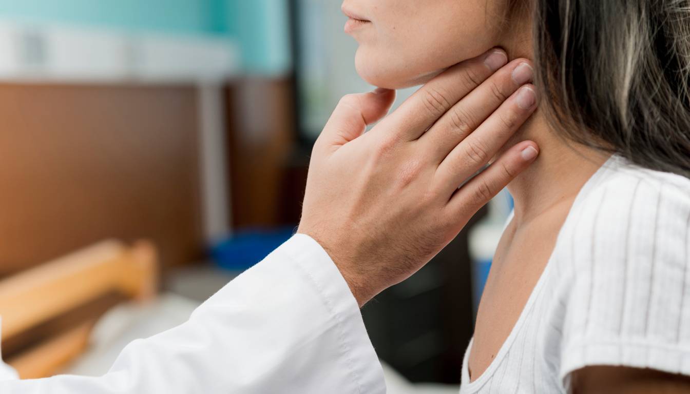 A doctor examines a patient's neck by gently pressing on the thyroid area.