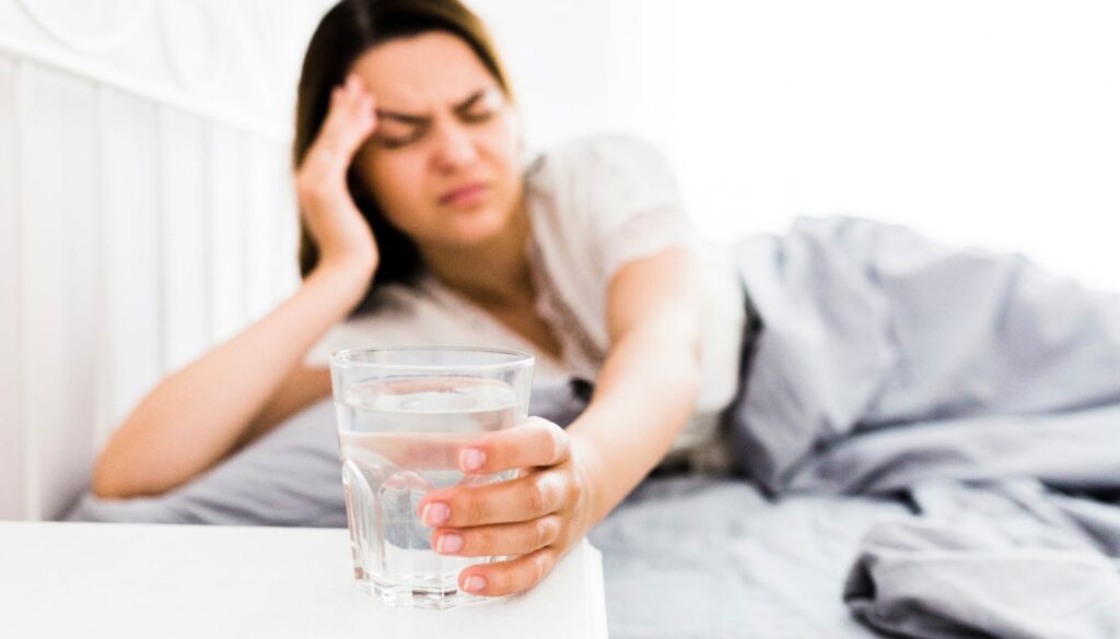 A close-up of a wooden table with vitamin supplements, a glass of water, and a slice of lemon, symbolizing hangover recovery essentials.