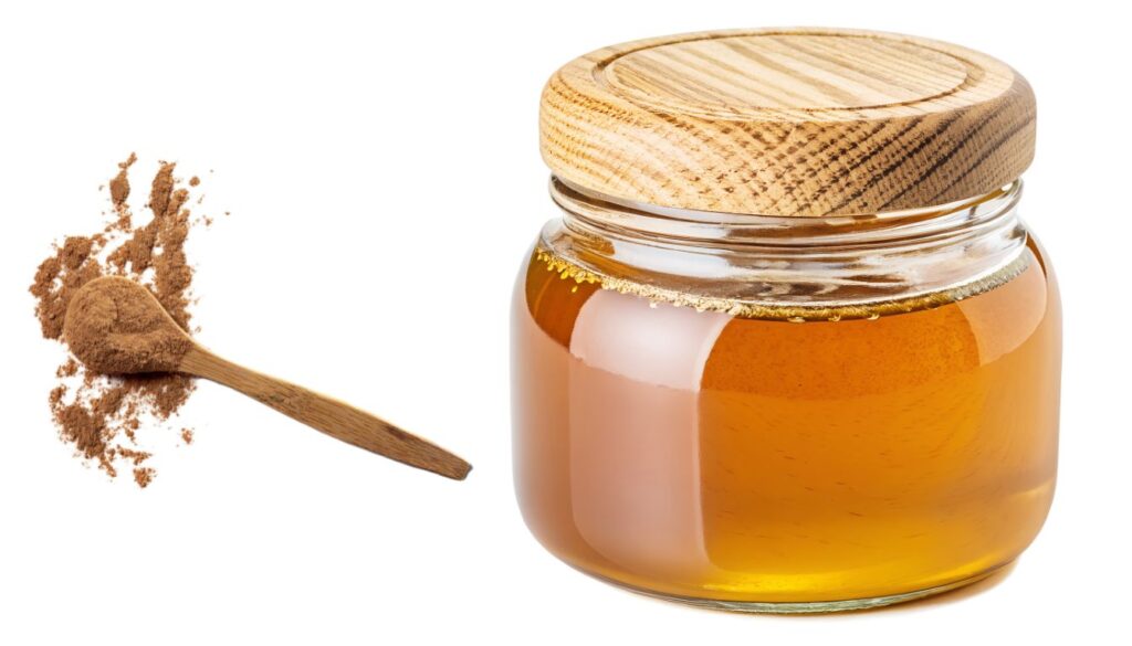 A jar of golden honey with a wooden dipper, placed next to a bowl of ground cinnamon on a wooden table, highlighting natural home remedies.