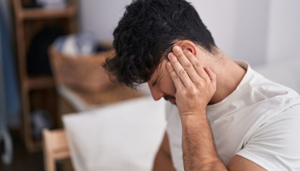 A person holding their left ear with their hand, depicting discomfort or the sensation of ringing.