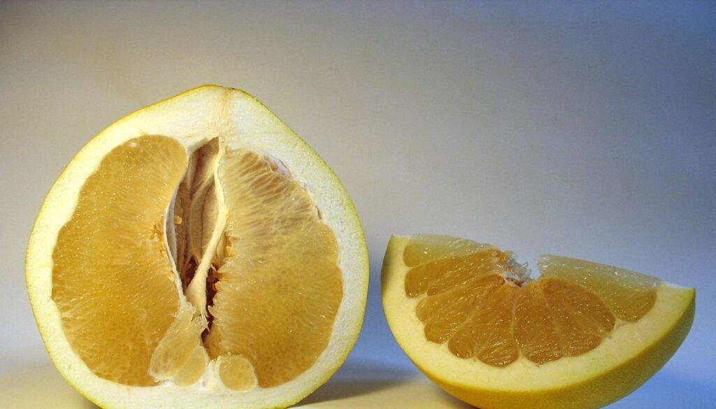 A vibrant pomelo fruit cut into halves, showcasing its juicy, segmented interior and thick rind on a wooden table surrounded by fresh greenery.