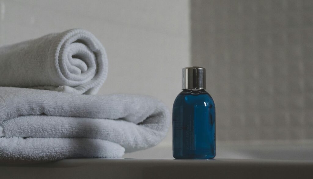 A compact blue bottle with a silver cap sitting beside neatly folded white towels on a bathroom counter.