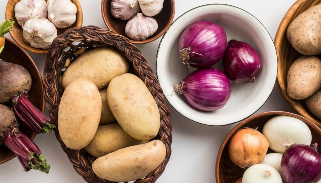 A selection of energy-boosting vegetables, including potatoes, garlic, onions, and beets, displayed in bowls and baskets on a white surface.