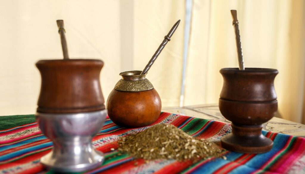"A steaming cup of yerba mate tea on a rustic table, surrounded by vibrant green leaves.