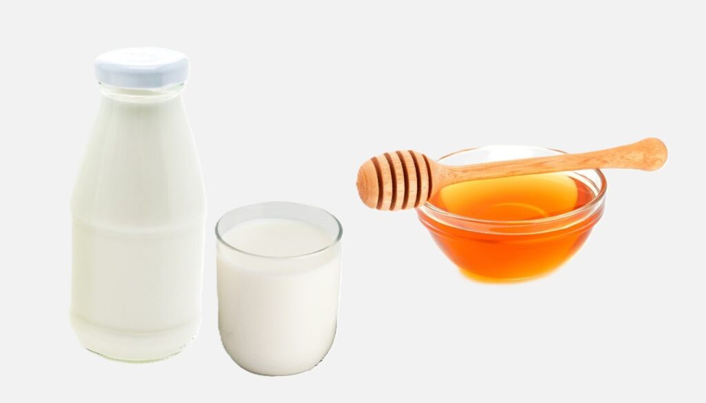 A rustic arrangement of a glass of milk, a jar of golden honey, and a wooden honey dipper on a wooden table.