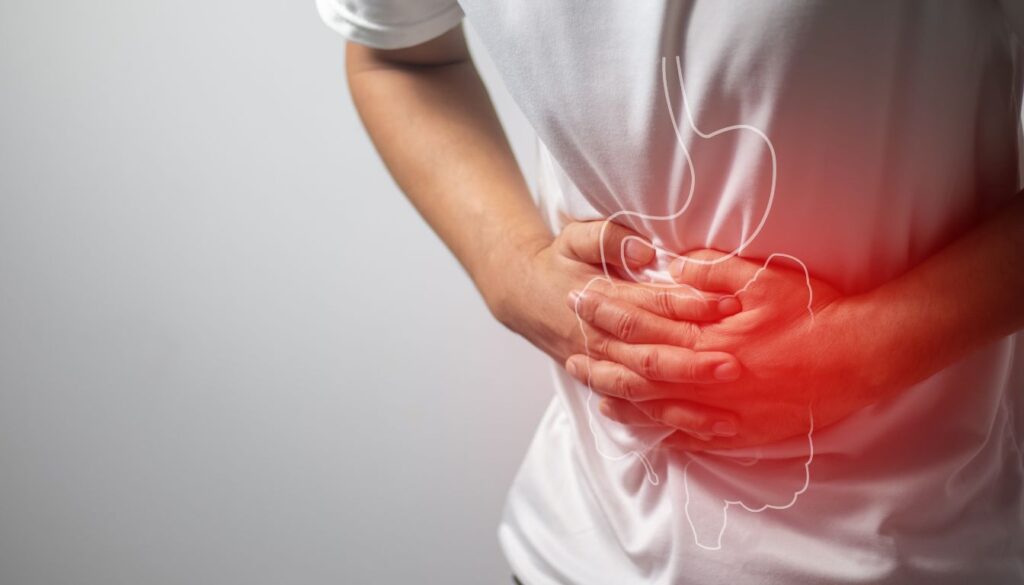 A person in a white shirt holding their stomach with both hands, indicating discomfort. The stomach area is highlighted in red, with an outline of the stomach and intestines superimposed.