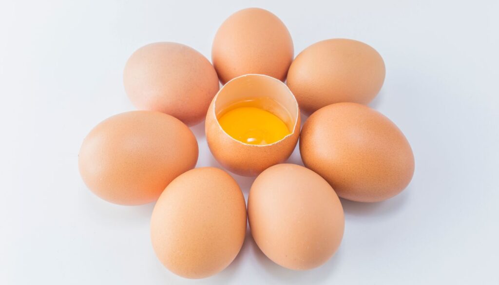 A close-up of raw eggs on a white surface, with one egg cracked open to reveal a vivid yellow yolk.