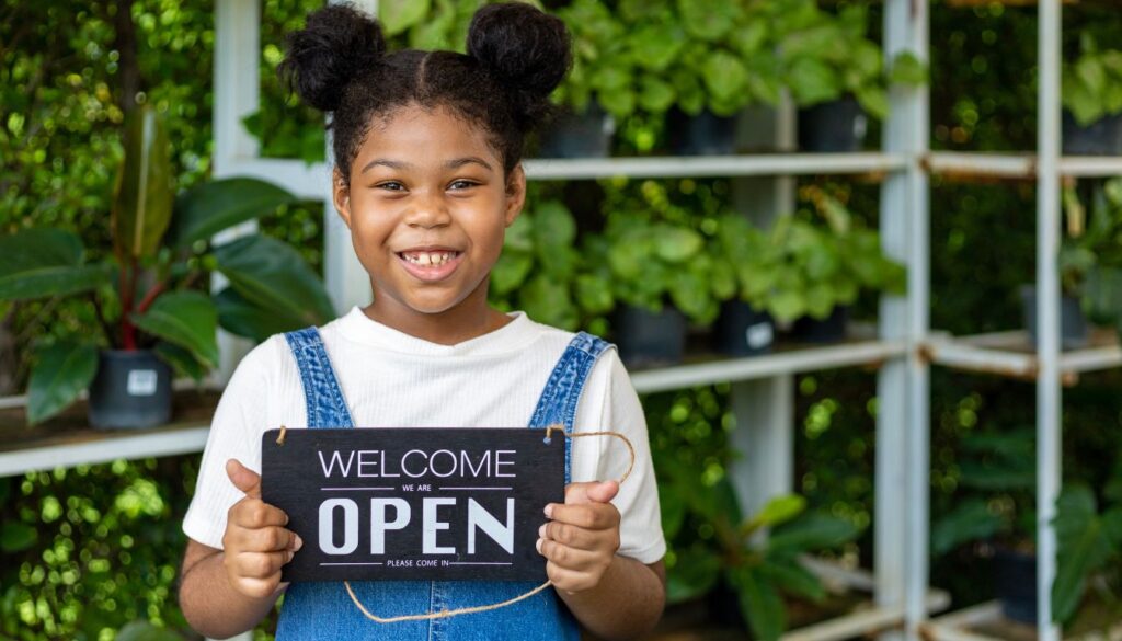 A young child painting a colorful flower pot outdoors, surrounded by garden tools and vibrant plants.