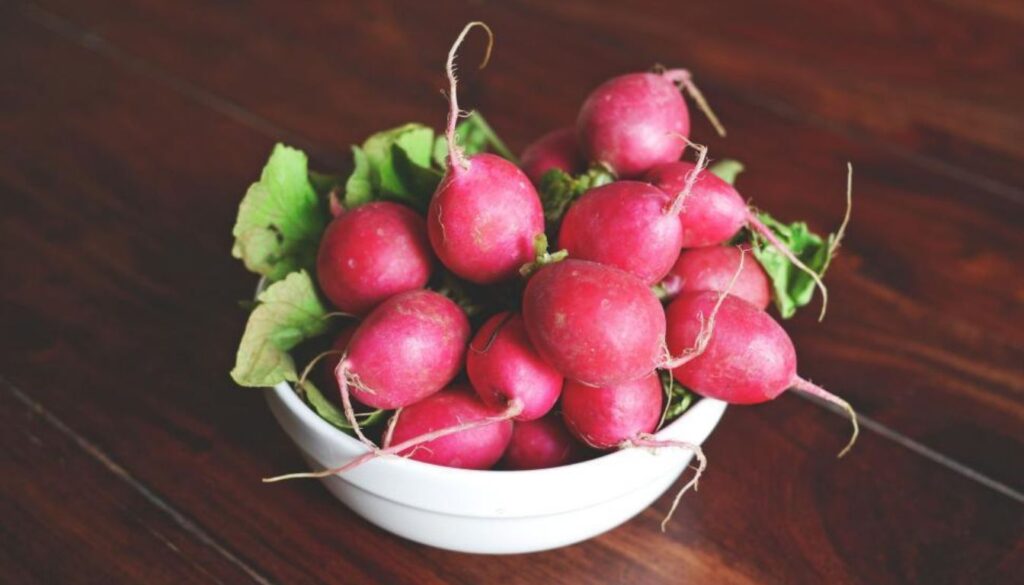 A vibrant bunch of fresh raw radishes with their green leafy tops, placed on a wooden cutting board, showcasing their crisp texture and bright red color.