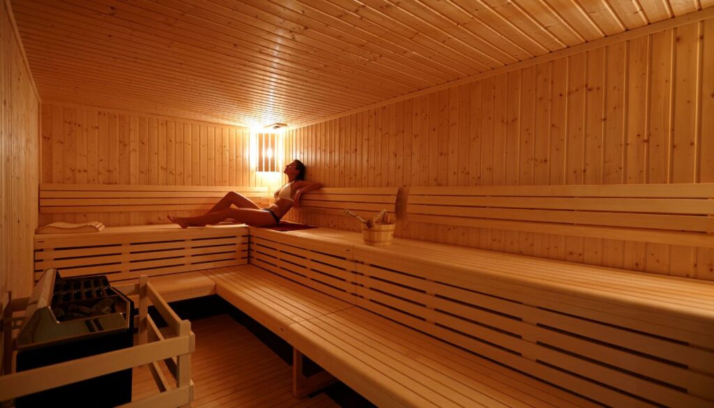 A person relaxing in a wooden sauna, sitting on a towel with soft lighting enhancing the warm atmosphere.