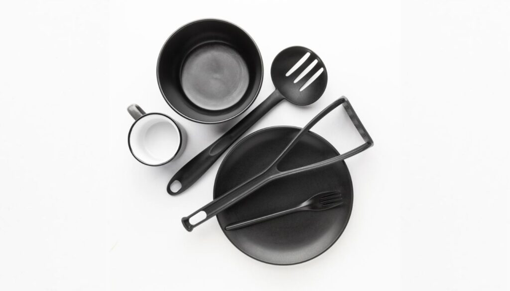 A collection of black silicone cookware, including a bowl, plate, mug, slotted spoon, spatula, and fork, neatly arranged on a white surface.