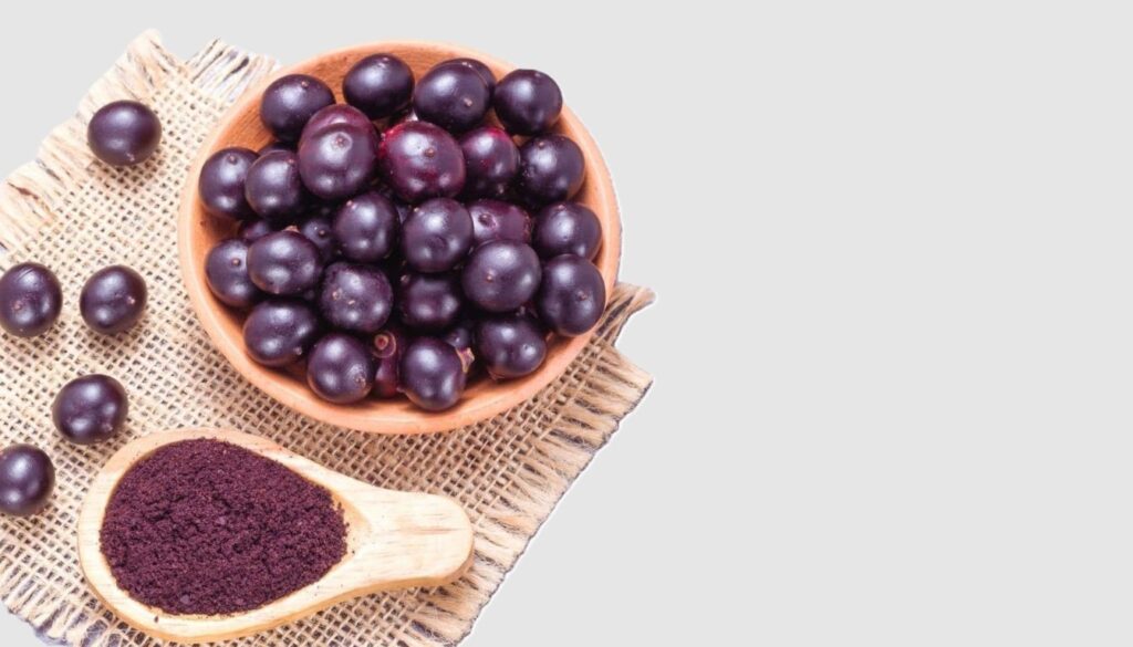 A rustic wooden bowl filled with vibrant acai berries resting on a burlap mat, with a wooden spoon dusted in acai powder.
