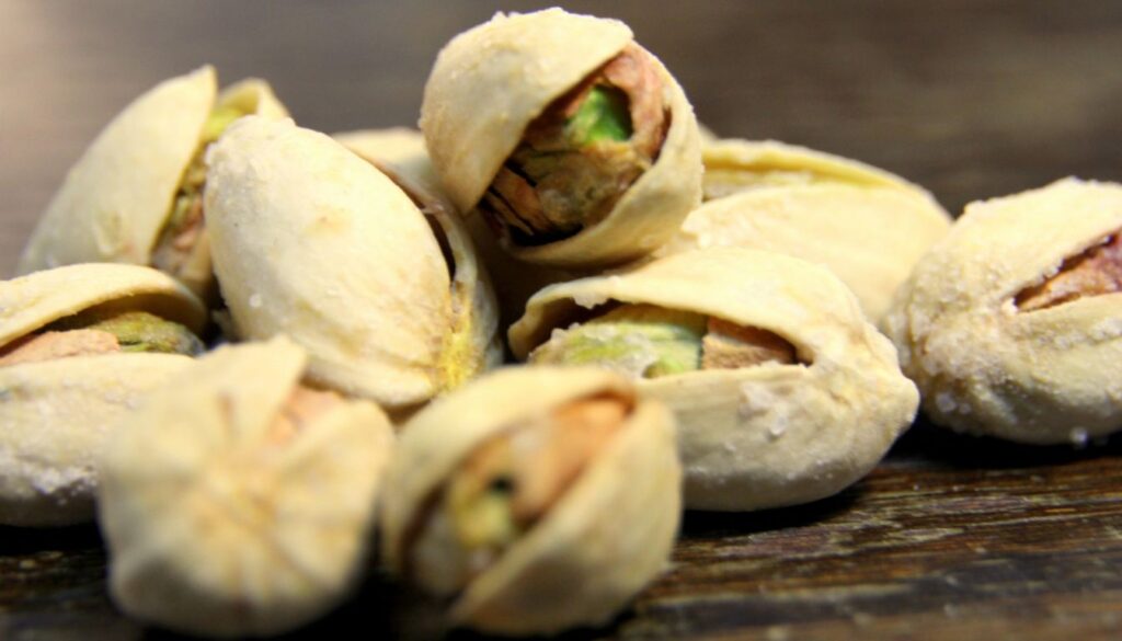 A close-up image of shelled pistachios in a bowl, showcasing their vibrant green and creamy texture, placed on a wooden table.