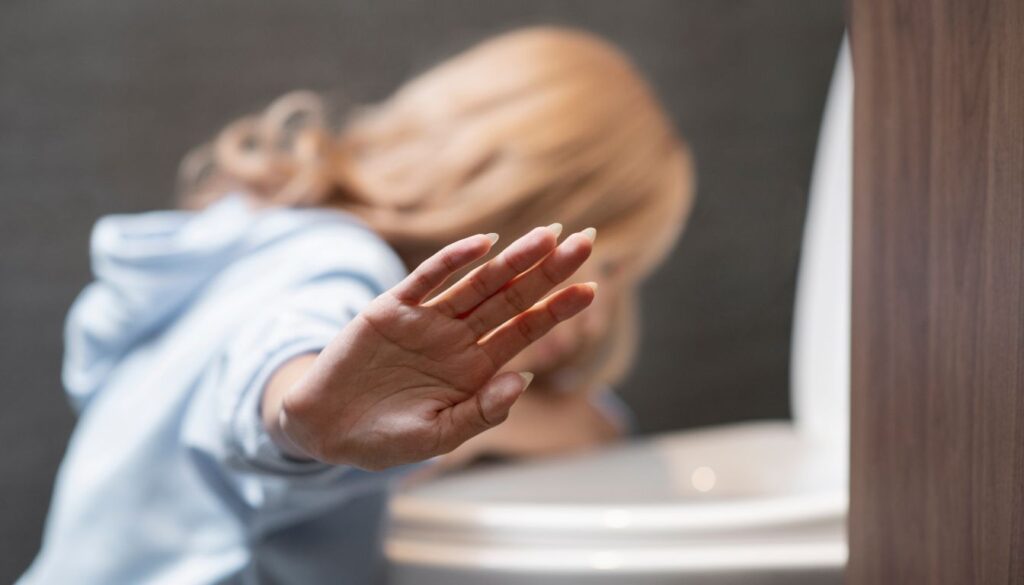 A person experiencing discomfort, leaning over a toilet sink symbolizing that suffers from vomiting bile.