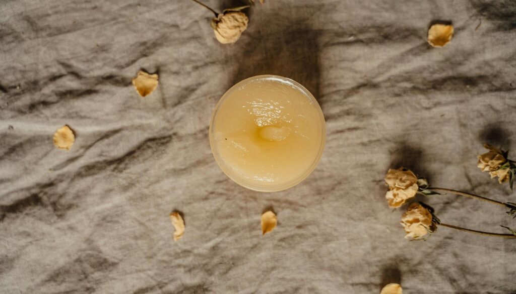 A top-view layout of natural ingredients including herbs, carrier oil, beeswax, and essential oils arranged on a clean kitchen counter, ready for DIY ointment making.