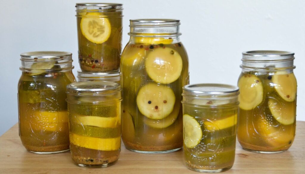 A jar of homemade zucchini pickles, with thinly sliced zucchini submerged in a golden brine, placed on a rustic wooden surface.