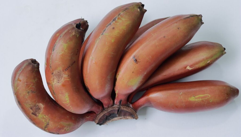 A vibrant bunch of red bananas with deep reddish peels arranged on a rustic wooden surface, highlighting their unique color and texture.