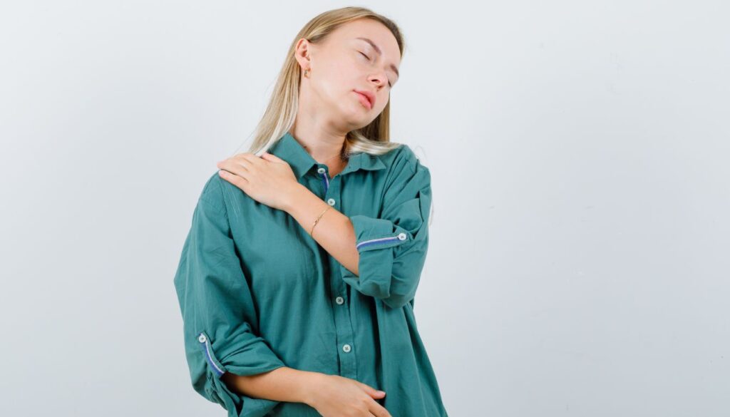 A pregnant woman gently holds her shoulder, her expression reflecting discomfort.