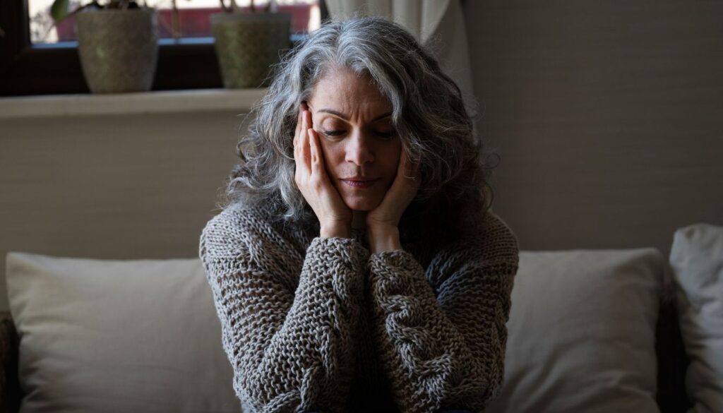 A mature woman in a softly lit, cozy living room, holding a warm cup of herbal tea and exuding calm and relief.