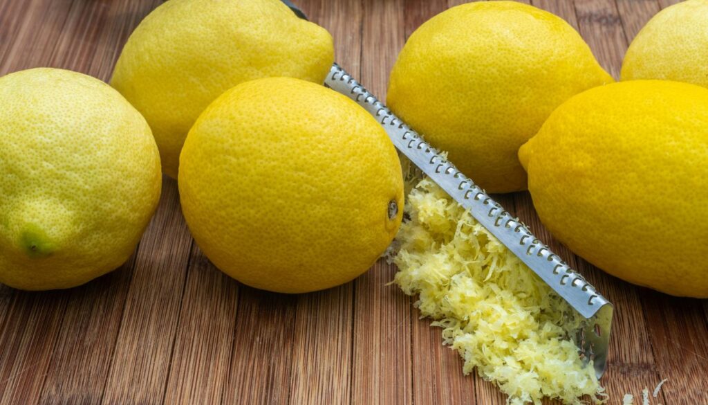 Close-up of freshly grated lime zest with whole limes and a wooden board.