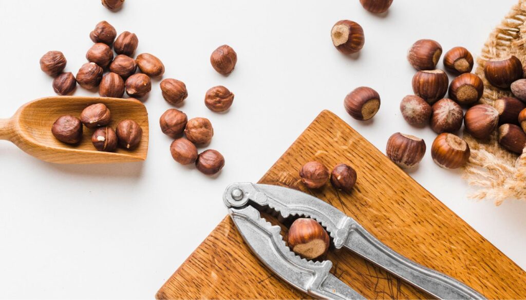 A close-up of a wooden bowl filled with hazelnuts, surrounded by scattered nuts on a rustic surface.