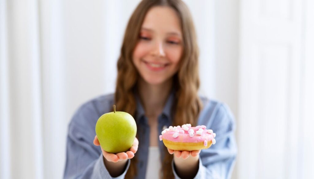 A young woman holding a donut in one hand and an apple in the other, appearing to choose the healthier option.