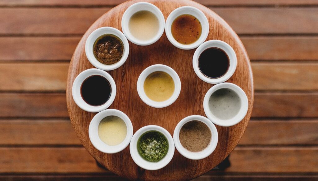 Assorted sauces in small white bowls arranged on a wooden surface.