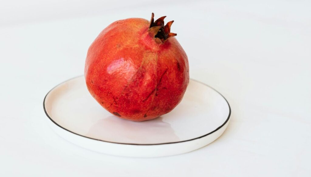 A vibrant display of fresh pomegranates, some whole and others cut open to reveal their juicy red seeds.