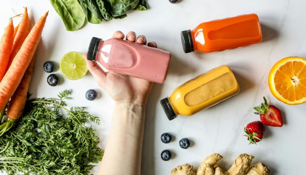 A clear glass filled with vibrant green juice, garnished with mint, surrounded by fresh fruits and vegetables.