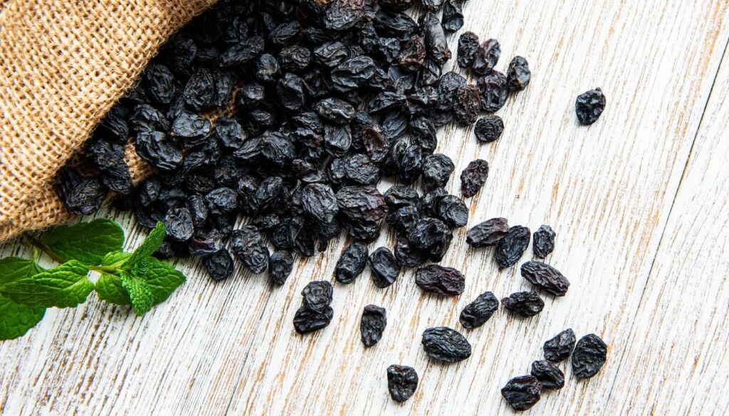 A wooden bowl filled with plump black raisins, highlighting their rich texture and deep color.