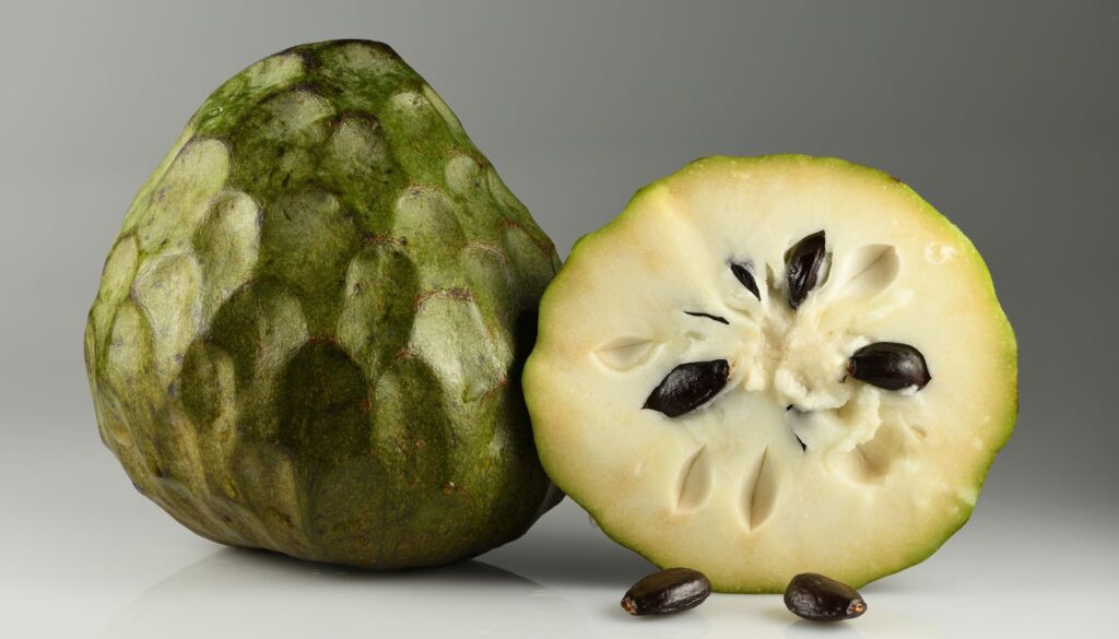 A fresh cherimoya fruit, sliced open to reveal its creamy white flesh and dark seeds, placed on a rustic wooden surface.