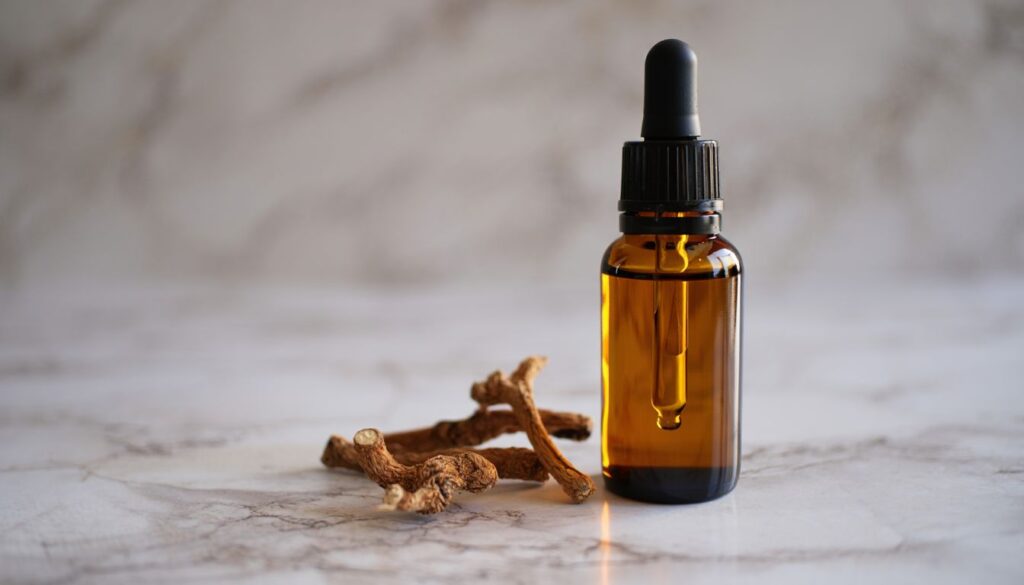 A small glass dropper bottle filled with a golden liquid, surrounded by dried valerian roots on a marble surface.