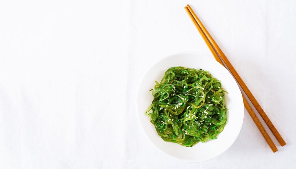A close-up of fresh edible seaweed with vibrant green and brown hues, showcasing its glossy texture and delicate, flowing strands.