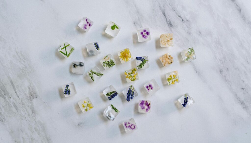 Assorted herbal ice cubes with colorful flowers and herbs frozen inside, arranged on a marble surface.