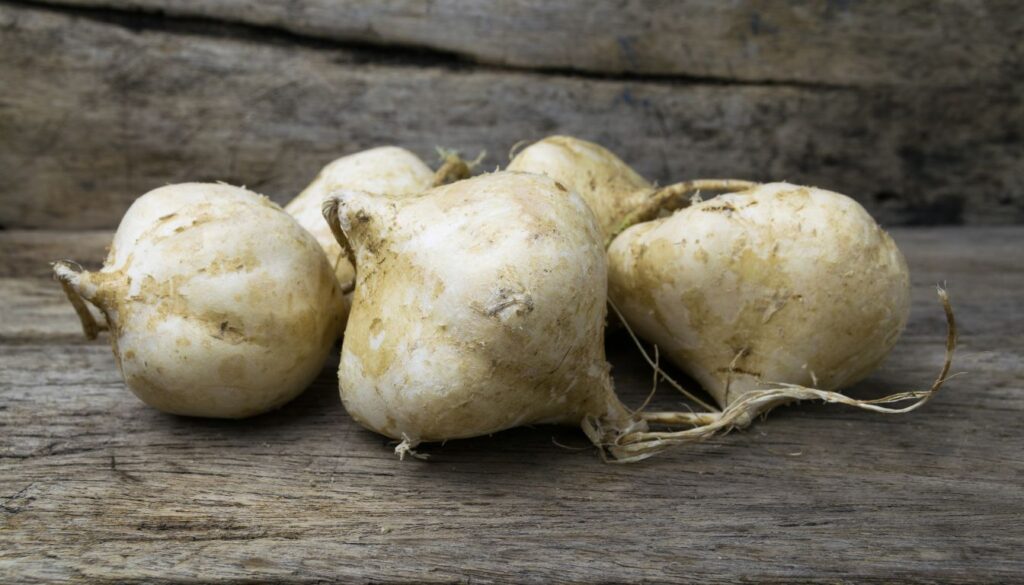 Five fresh jicamas resting on a wooden table, showcasing their smooth, earthy skin and natural texture.