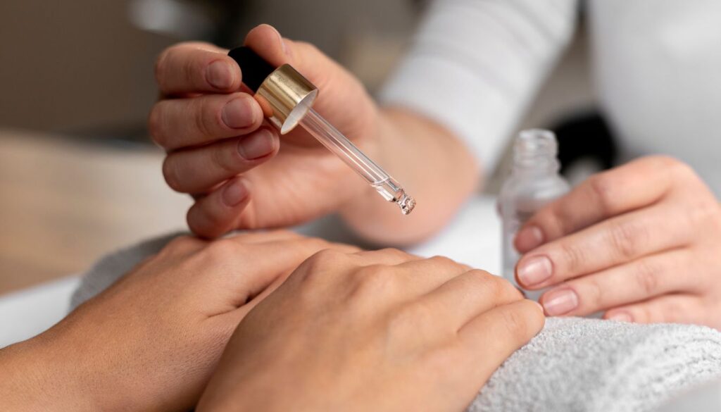Close-up of hands applying herbal nail oil with a dropper onto clean nails, resting on a soft towel.