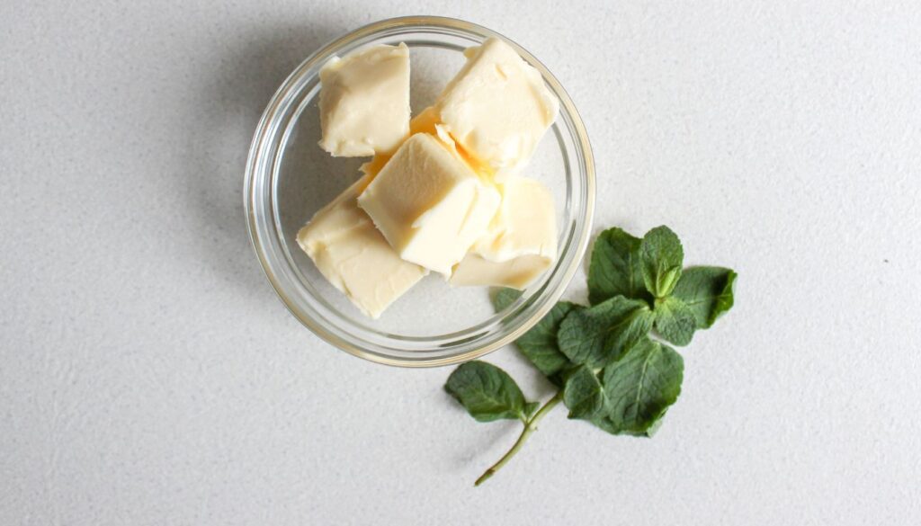A glass bowl filled with margarine cubes, accompanied by a fresh mint leaf for contrast.