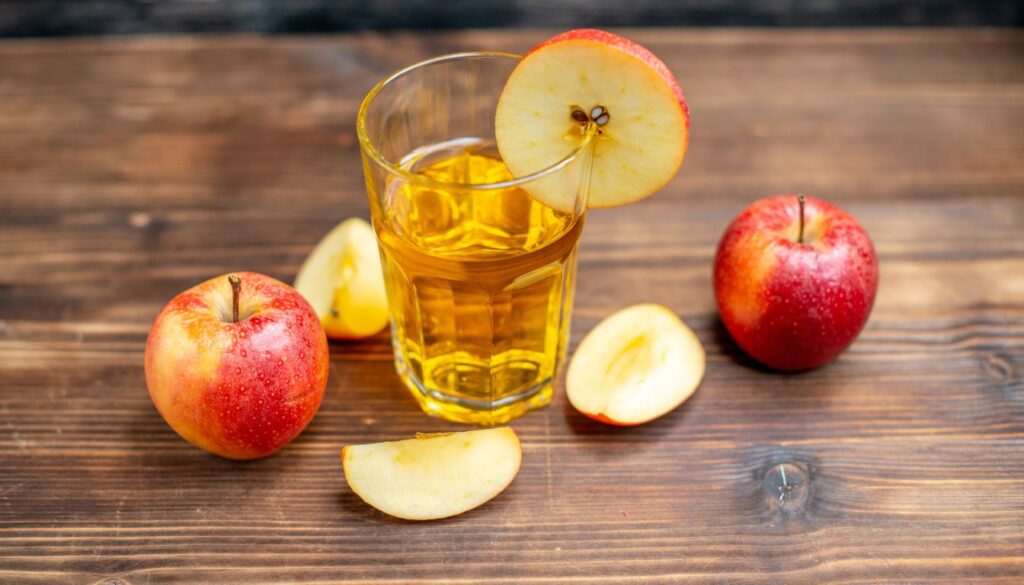 A glass of fresh apple juice with whole and sliced apples, highlighting its natural freshness and health benefits.