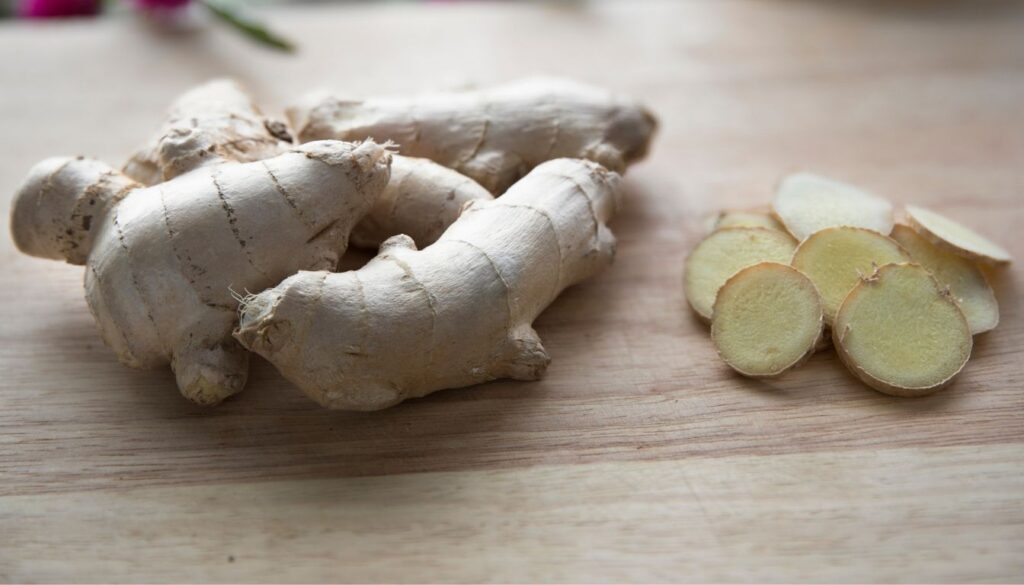 Fresh ginger root and sliced pieces on a wooden surface, showcasing its fibrous texture and pale yellow interior.