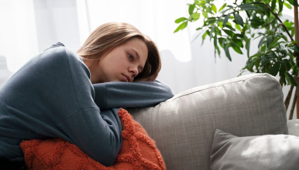 Person resting on a couch with a red-orange blanket and a green plant in the background.
