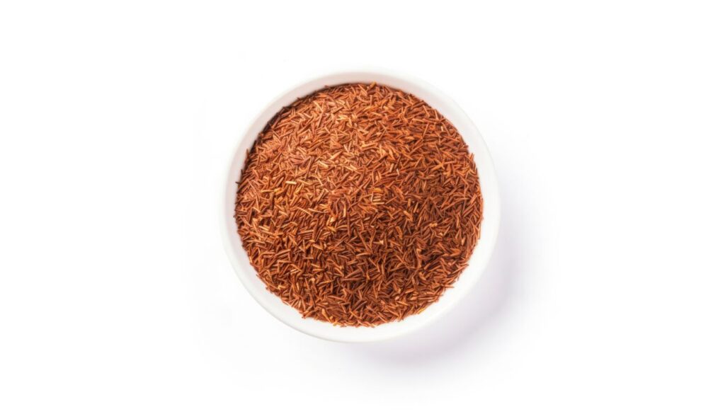 Reddish-brown rooibos tea leaves in a white bowl, showcasing their needle-like texture.