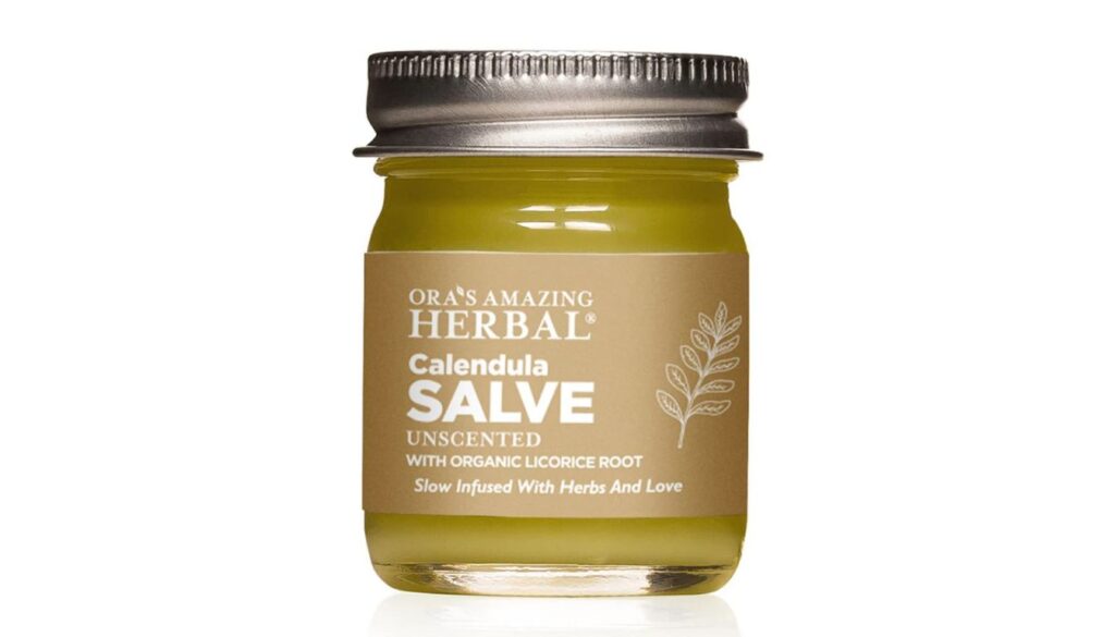 Jar of Ora's Amazing Herbal Calendula Salve with tan label and metallic lid, surrounded by natural elements.
