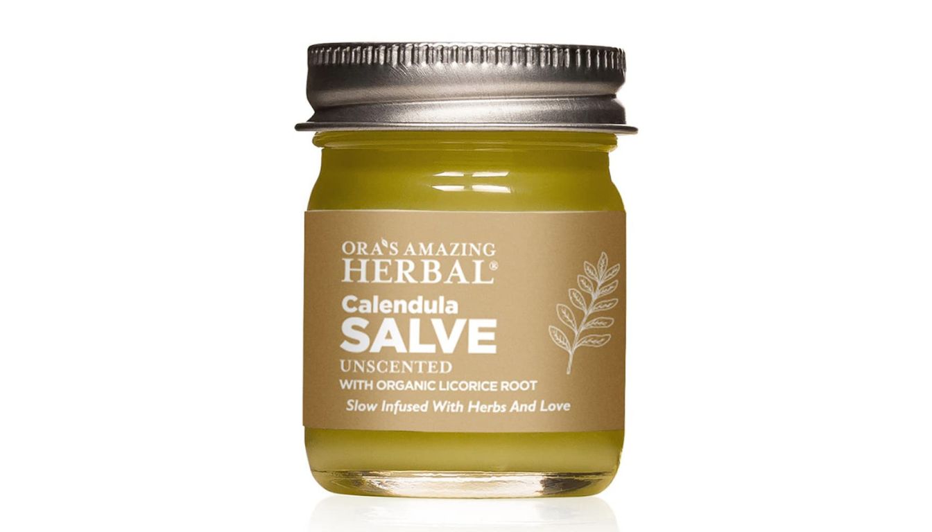 Jar of Ora's Amazing Herbal Calendula Salve with tan label and metallic lid, surrounded by natural elements.